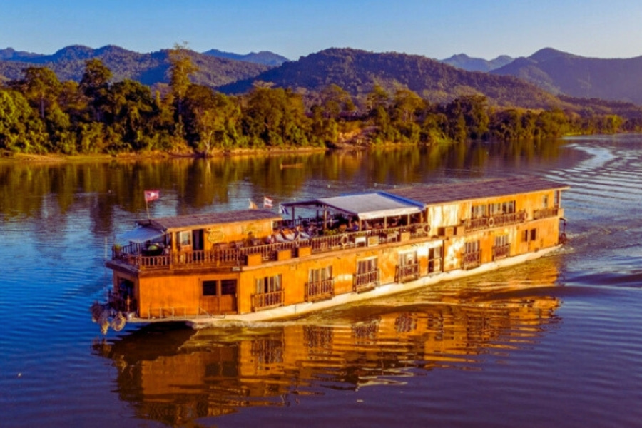 Wooden Mekong River cruise ship in Laos sailing past forested mountains